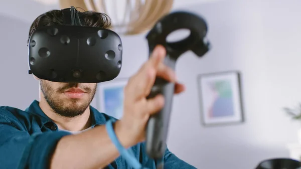 Jovem Energético Vestindo Headset Realidade Virtual e Segurando Controladores Joga em um Jogo de Vídeo em casa. Homem ativo jogando VR Quest Aventura Videogame no meio da sala de estar. — Fotografia de Stock