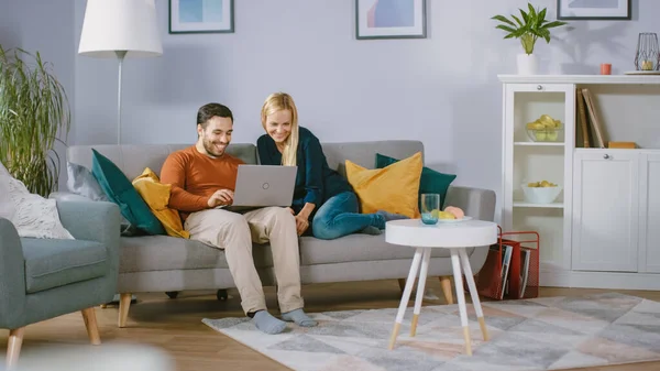 Boldog pár ül egy kanapén otthon, barátja tartja Laptop térden, Böngészés az interneten, csinál e-Shopping, használata Streaming Services. Boldog család a kényelmes nappaliban. — Stock Fotó