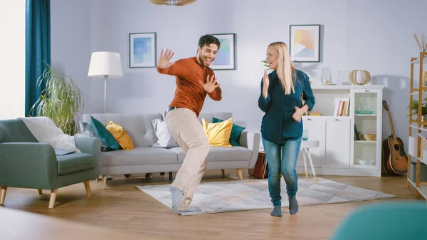 Hermosa pareja joven feliz en el amor bailando en medio de la sala de estar. Novio y novia celebran alegremente bailando en casa. — Foto de Stock