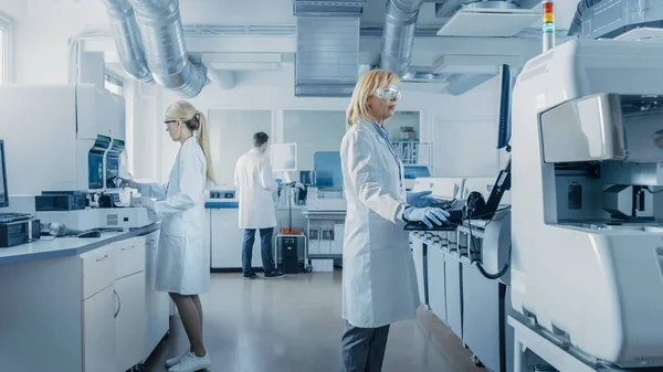 Forskargrupp som arbetar med dator, medicinsk utrustning, analys av blodprover och genetiska material med specialmaskiner i det moderna laboratoriet. — Stockfoto