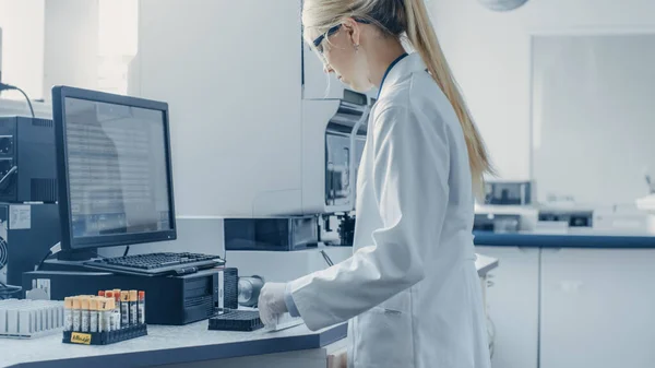 У біотехнологічній лабораторії Жіночий науковий співробітник аналізує пробірку в медичній машині, працює з кров'ю, зразки генетичного матеріалу . — стокове фото