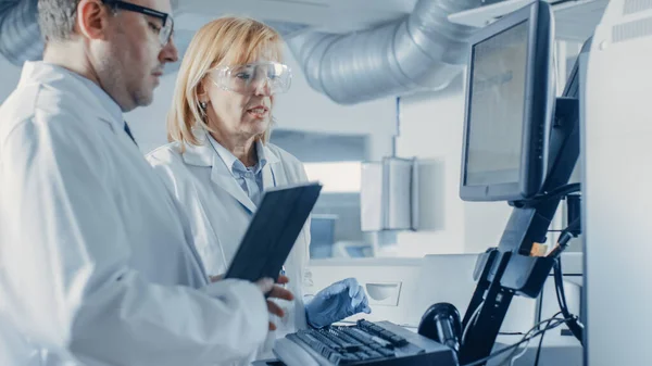 Zwei Forscher programmieren medizinische Geräte mit Tablet-Computern. Team von Fachleuten für pharmazeutische Forschung im modernen Labor. — Stockfoto