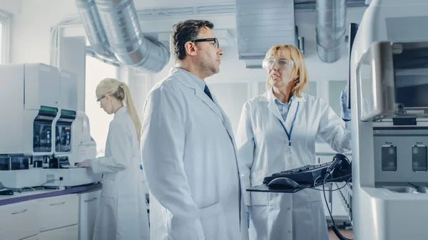 Två forskare talar om programmering medicinsk utrustning för tester. Team of Professionals gör farmaceutisk forskning i moderna laboratoriet — Stockfoto