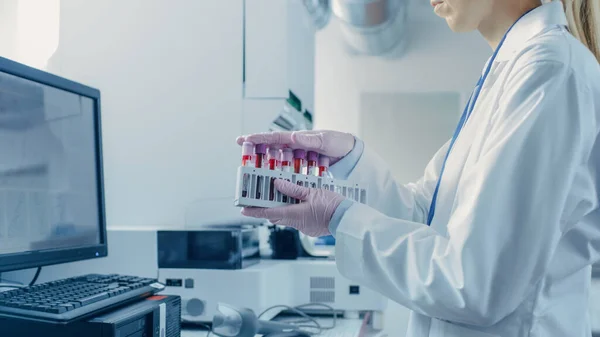 女性研究科学家在将血液样本放入分析仪的医疗机器之前，先持有带血样的试管。制药实验室现代医疗设备的科学家工作. — 图库照片