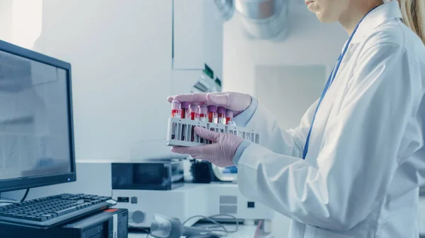 Vrouwelijke Research Scientist houdt reageerbuizen met bloedmonsters voordat ze in Analyzer Medical Machine. Wetenschapper werkt met moderne medische apparatuur in farmaceutisch laboratorium. — Stockfoto