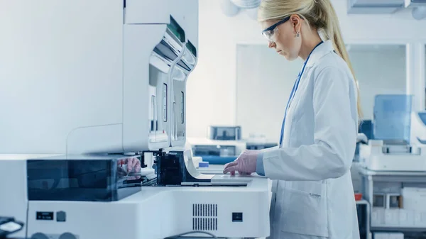 Жінка-дослідник вводить пробні трубки з зразками крові в аналізатор медичної машини. Вчений працює з сучасним медичним обладнанням у фармацевтичній лабораторії . — стокове фото
