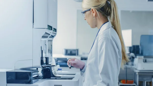 Female Research Scientist Places Test Tube met bloedmonster in medische analyseapparatuur. Wetenschapper werkt in een modern farmaceutisch laboratorium. — Stockfoto