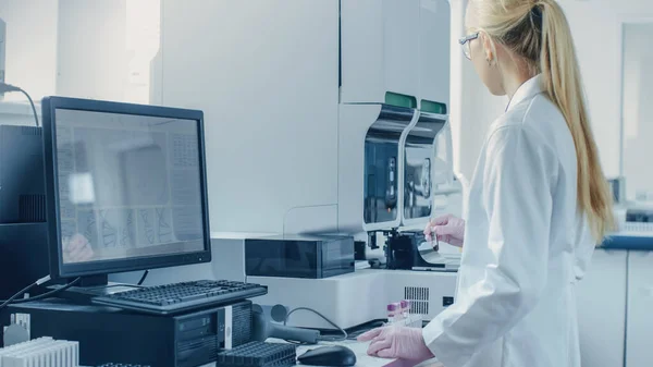 Forscherin arbeitet mit medizinischer Analysemaschine zur Untersuchung von Röhrchen mit Blutprobe. Wissenschaftler arbeitet in innovativem Labor für pharmazeutische Genforschung. — Stockfoto
