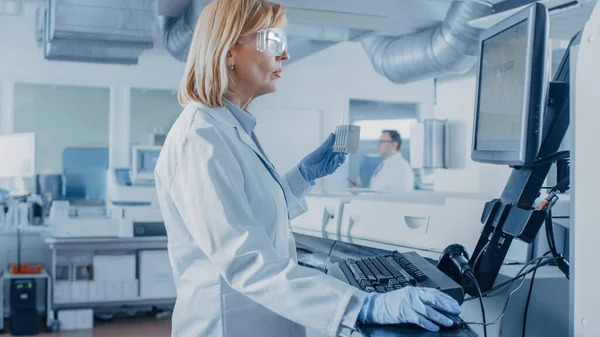 In laboratorio la scienziata donna analizza i dati della provetta con i campioni di sangue con il personal computer. Team di ricercatori che lavorano nel laboratorio farmaceutico. — Foto Stock