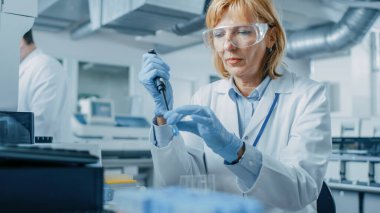 Kadın araştırmacı bilim adamı test tüpleri üzerinde çalışırken mikro boru kullanıyor. Modern Tıbbi Genetik Araştırma Ekipmanı ile Yenilikçi İlaç Laboratuvarındaki İnsanlar.