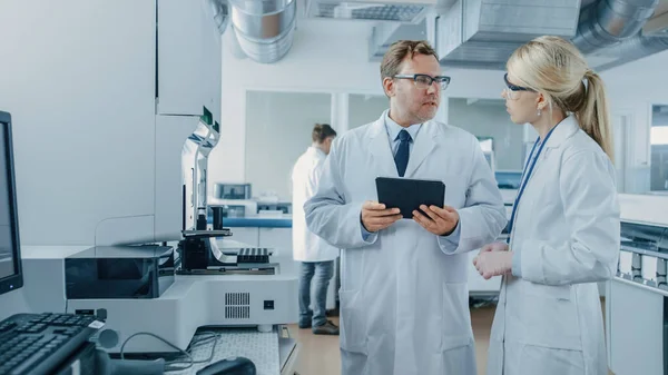 Wissenschaftlerinnen und Wissenschaftler im Gespräch, mit digitalem Tablet-Computer während der Arbeit an einem Forschungsprojekt zur Genetik im innovativen Labor. — Stockfoto