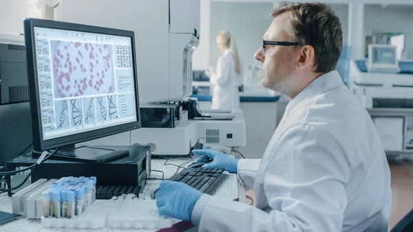 Férfi tudós ül a munkahelyén a laboratóriumban, használja a személyi számítógépet. A képernyőn DNS elemzés látható. I A Háttér Genetikai Kutatóközpont innovatív berendezésekkel. — Stock Fotó