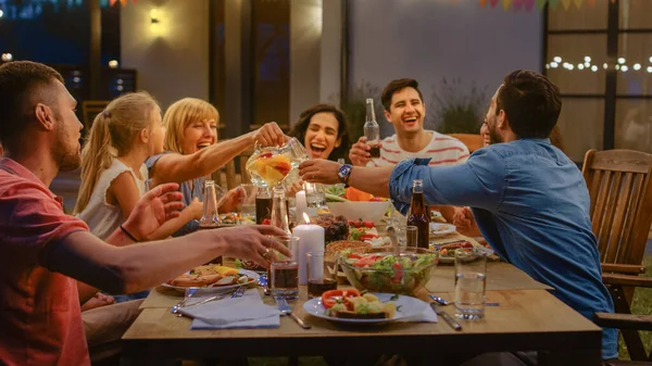 Gruppe av venner samlet seg ved bordet, slektninger og venner, unge og eldre spiste, drakk, passerte retter, Joking og hadde det moro. Hagefest Kveldsfest. – stockfoto