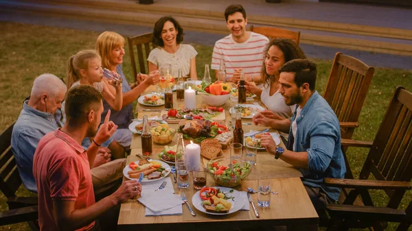 Groep vrienden verzameld aan de tafel Familieleden en vrienden, jong en oud zijn eten, drinken, passeren van gerechten, grapjes maken en plezier hebben. Tuinfeest Avondfeest. — Stockfoto