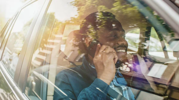 Schöner Jungunternehmer, der auf dem Beifahrersitz eines Autos sitzt, telefoniert, spricht mit Kunden oder Verwandten. Kamerafahrt von außerhalb des Fahrzeugs. — Stockfoto