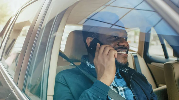 Joven emprendedor guapo viajando en un coche, sentado en un asiento de pasajeros hace una llamada telefónica, habla con clientes o familiares. Cámara disparada desde el exterior del vehículo. —  Fotos de Stock