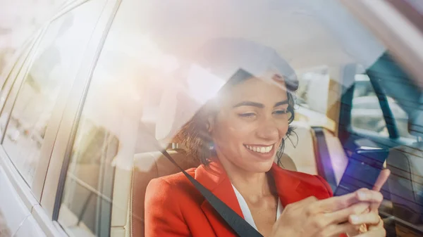 Gyönyörű nő Utazás autóban, Ül az utasülésen használja okostelefon, típusok Üzenet, Böngészés az interneten keresztül. Fényképezőgép a járművön kívülről. — Stock Fotó