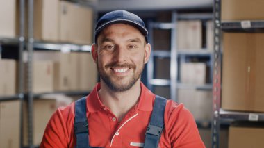 Gülümseyen Üniformalı İşçi Portresi. Arka planda, raflarla dolu karton paketlerle dolu bir oda nakliyeye hazır..