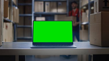 Green Mock-up ekranlı dizüstü bilgisayar Man 'in çalıştığı depodaki Masaüstünde duruyor.