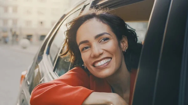 Lykkelig, vakker kvinne som kjører i en bil, ser ut av det åpne vinduet i Storbyens underverk. Reisende jente opplever magi fra hele verden. Skutt fra utsiden av kjøretøyet. – stockfoto