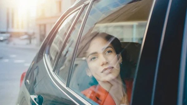 Beautiful Sad Woman Rides on a Passenger Back Seat of a Car, Looks out of the Window Dreamily. Big City View Reflects in the Window. Camera Mounted outside Moving Car.