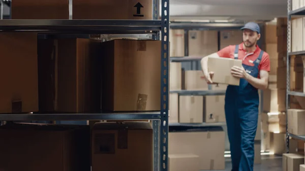 Trabajador de almacén guapo entra en el almacén con una caja de cartón. — Foto de Stock
