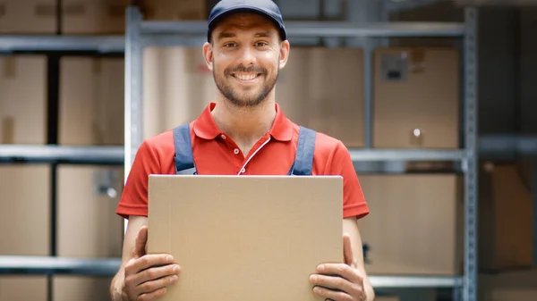 Trabajador de almacén guapo en uniforme sostiene paquete de la caja de cartón y sonríe. — Foto de Stock
