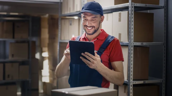 El trabajador del almacén utiliza la tableta digital para comprobar el stock, en las cajas de cartón de pie de los estantes. — Foto de Stock