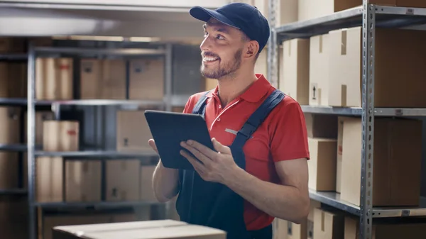 El trabajador del almacén utiliza la tableta digital para comprobar el stock, en las cajas de cartón de pie de los estantes. — Foto de Stock