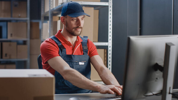Portrait of Uniformed Worker Using Personal Computer while Sitting at His Desk in the Warehouse.