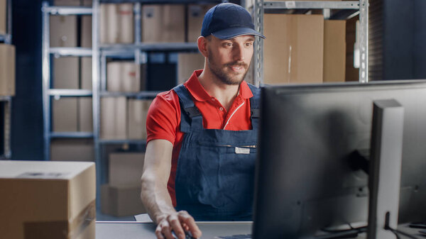 Portrait of Uniformed Worker Using Personal Computer while Sitting at His Desk in the Warehouse.