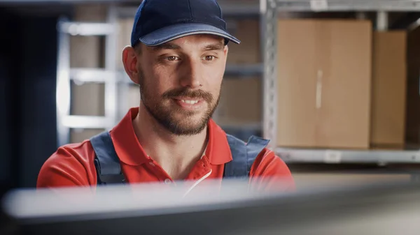 Primer plano de un trabajador uniformado usando una computadora personal mientras está sentado en su escritorio en el almacén. — Foto de Stock