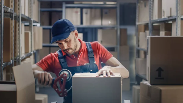 Profesional Warehouse Worker termina la orden, sellando cajas de cartón listas para el envío. En las filas de fondo de estantes con cajas de cartón con pedidos listos. — Foto de Stock