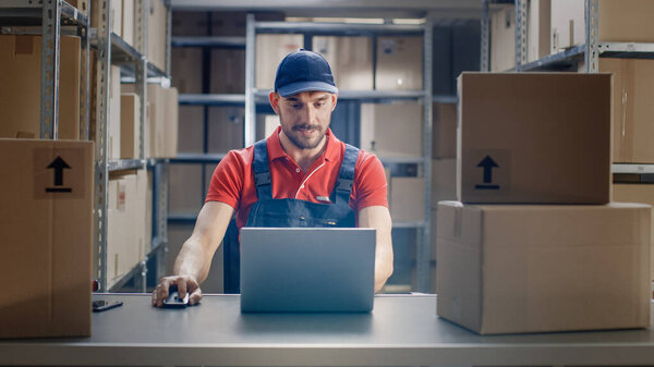 Uniformed Worker Uses Laptop while Sitting at His Desk in the Warehouse.