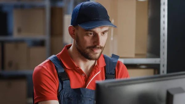 Retrato del trabajador uniformado usando una computadora personal mientras está sentado en su escritorio en el almacén. — Foto de Stock