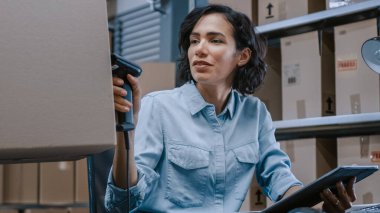 Kadın Envanter Müdürü Karton Kutu ve Barkod Tarayıcı ile Dijital Tablet, İşçi Tutucu Paketi. Karton Kutuların Arkaplan Sıralarında Ürünler Nakliyeye Hazır.