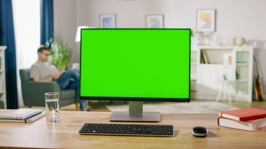 Green Mock-up Screen Standing on the Desk ile Modern Kişisel Bilgisayar. Konforlu ve aydınlık oturma odasında kitap okuyan bir sandalyede dinleniyor..