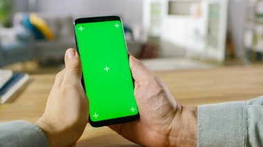 Modern Green Mock-up Akıllı Telefonu Elinde Tutan Bir Adam 'ın Yakın Çekimi. Modern yüksek kalite cihaz kullanılıyor. Oturma odasında ya da İçişleri Bakanlığı 'nda..