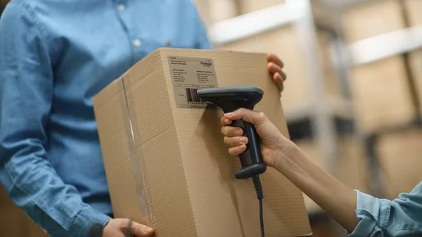 Female Inventory Manager Scans Kartonnen doos en met Barcode Scanner, Mannelijke werknemer houdt Pakket. Op de achtergrond rijen van Kartonnen dozen met producten klaar voor verzending. — Stockfoto