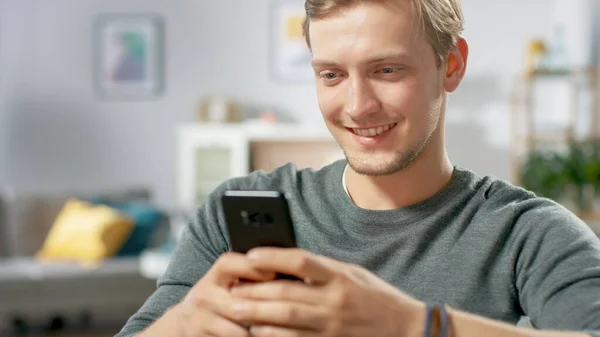 Porträt des hübschen jungen Mannes, der Smartphone benutzt, im Internet surft, soziale Netzwerke checkt, während er zu Hause sitzt. — Stockfoto