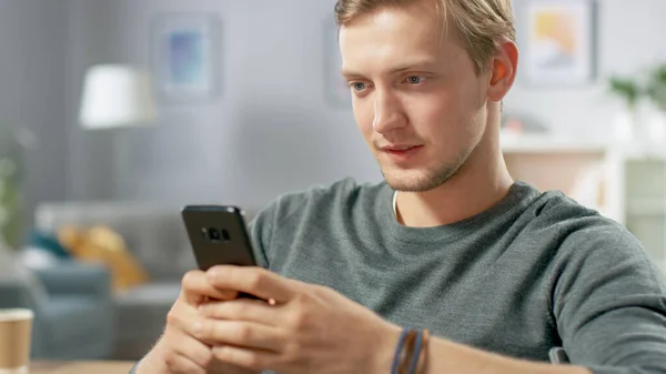 Komean nuoren miehen muotokuva Älypuhelimen käyttö, Internetin selaaminen, sosiaalisten verkostojen tarkistaminen kotona istuessa. — kuvapankkivalokuva