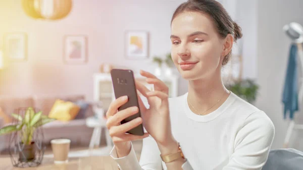 Porträt der schönen jungen Frau, die Smartphone benutzt, im Internet surft, soziale Netzwerke checkt, während sie zu Hause sitzt. — Stockfoto
