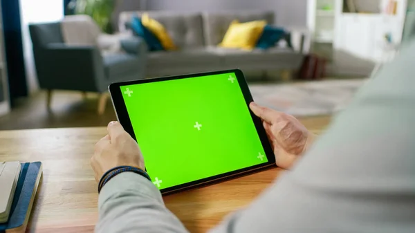 Man Holding and Watching Green Mock-up Screen Digital Tablet Computer While Sitting at the Desk. Man Watching Videos or Browsing Through the Internet. In the Background Cozy Living Room. — Stock Photo, Image