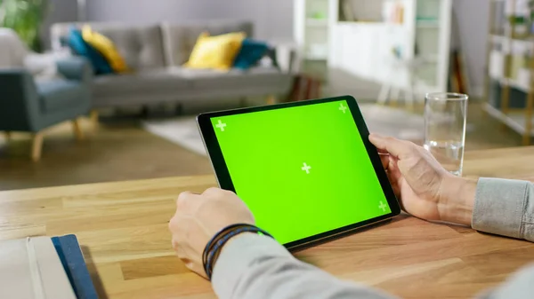 Man Holding Green Mock-up Screen Digital Tablet Computer Enquanto sentado na mesa. Homem a comprar coisas ou a navegar pela Internet. No fundo aconchegante sala de estar. — Fotografia de Stock