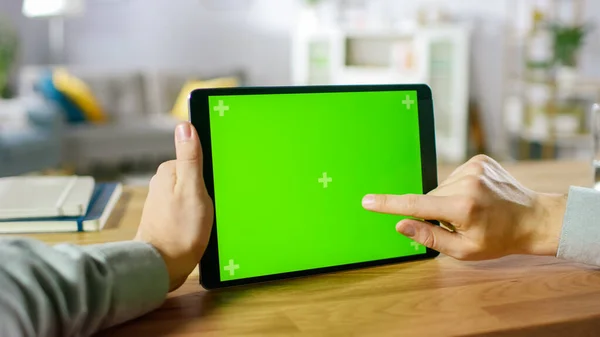 Nahaufnahme des Menschen mit Handgesten auf grünem Mock-up Screen Digital Tablet Computer im Landscape-Modus, während er an seinem Schreibtisch sitzt. Im Hintergrund gemütliches Wohnzimmer. — Stockfoto