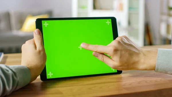 Close-up of Man Using Hand Gestures on Green Mock-up Screen Digital Tablet Computer in Landscape Mode while Sitting at His Desk. In the Background Cozy Living Room. — Stock Photo, Image