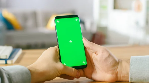 Közelkép egy férfiról, aki zöld Mock-up Screen Smartphone-t tart a kezében. Modern High End készüléket használ. A háttérben Hangulatos nappali vagy Home Office. — Stock Fotó