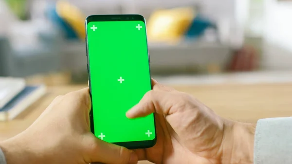 Gros plan d'un homme utilise un smartphone vert à écran maquillé et fait des gestes à l'écran tactile. Toucher téléphone portable Chroma écran clé. En arrière-plan Ambiance chaleureuse et chaleureuse. — Photo