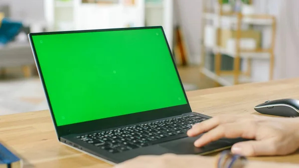 Homem usa laptop com tela de Mock-up verde enquanto sentado na mesa em sua acolhedora sala de estar. — Fotografia de Stock