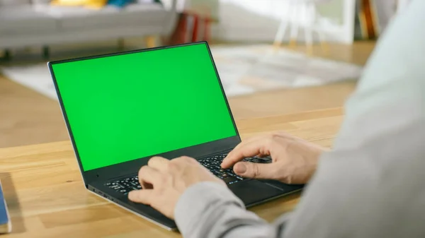 Freelancer Profissional Trabalha em um Laptop com Tela Mock-up Verde enquanto está sentado na mesa em sua acolhedora sala de estar. — Fotografia de Stock